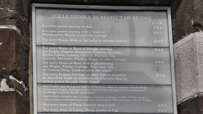 A black sign with white print detailing the toll fees to cross the Conwy Suspension Bridge, Conwy.
